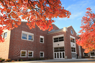 Image of the exterior of the CMU College of Medicine building in the background with two trees with orange and red leaves in the foreground.