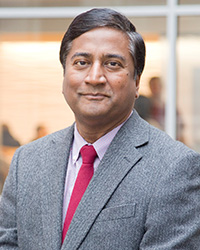 Dr. Sethu K Reddy smiles at the camera while wearing a gray suit coat and red tie.