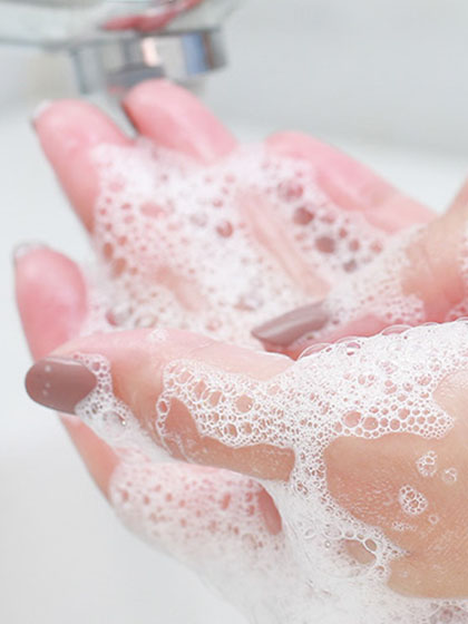 A feminine hand covered in soap suds during hand washing.