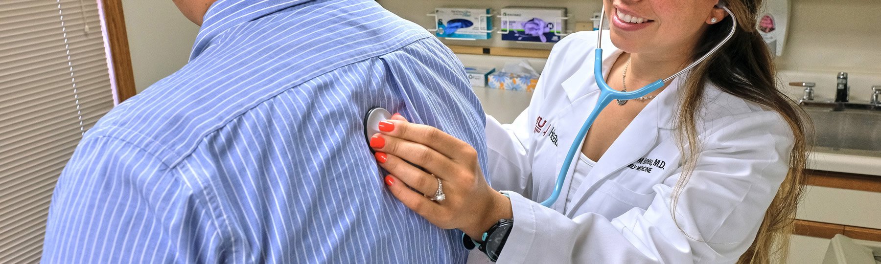 Doctor holding a stethoscope against a patient's back.