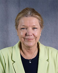 Woman wearing light green suit jacket with black shirt smiling.