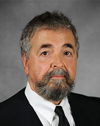 Man with salt and pepper beard wearing a black suit jacket, white shirt and a black tie.