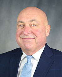 A man in a navy suit and light blue tie.